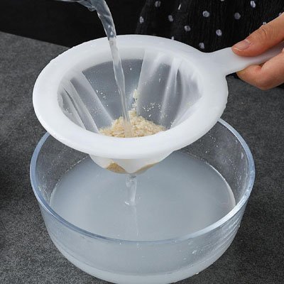 bol en vitre sur comptoir gris et homme tablier noir pois blanc filtrant liquide clair avec passoire 