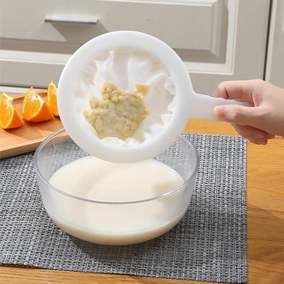 napperon gris sur comptoir bois avec quartier orange passoire grumeaux et bol de liquide blanc 