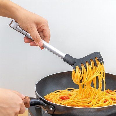 pince de cuisine dans poele avec nouilles jaunes et tomates